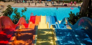 Na zdjęciu widać pięć kolorowych zjeżdżalni wodnych po których zjazd zakończony jest w wodzie. w tle widać ludzi za basenem. Zdjęcie prawdopodobnie jest zrobione w parku wodnym.