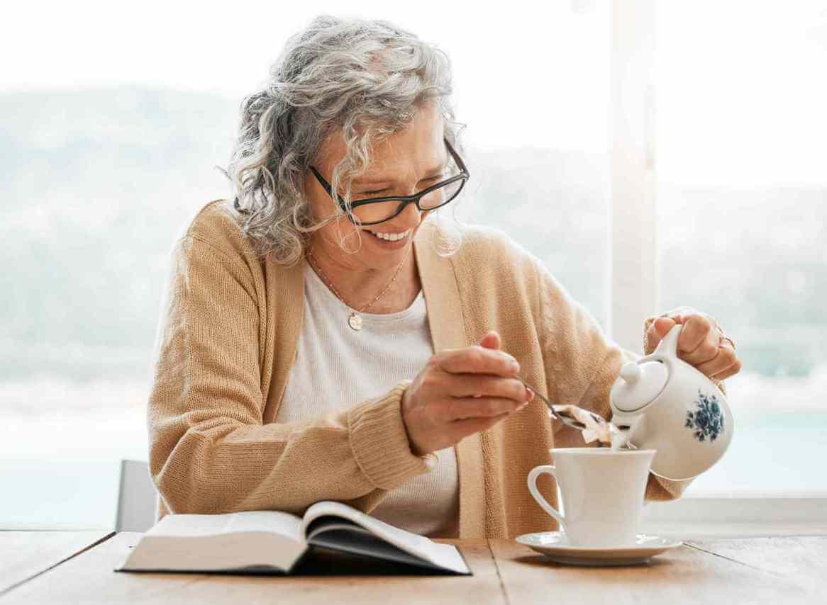 kobieta czytająca książki katolickie z uśmiechem zalewająca sobie herbatę